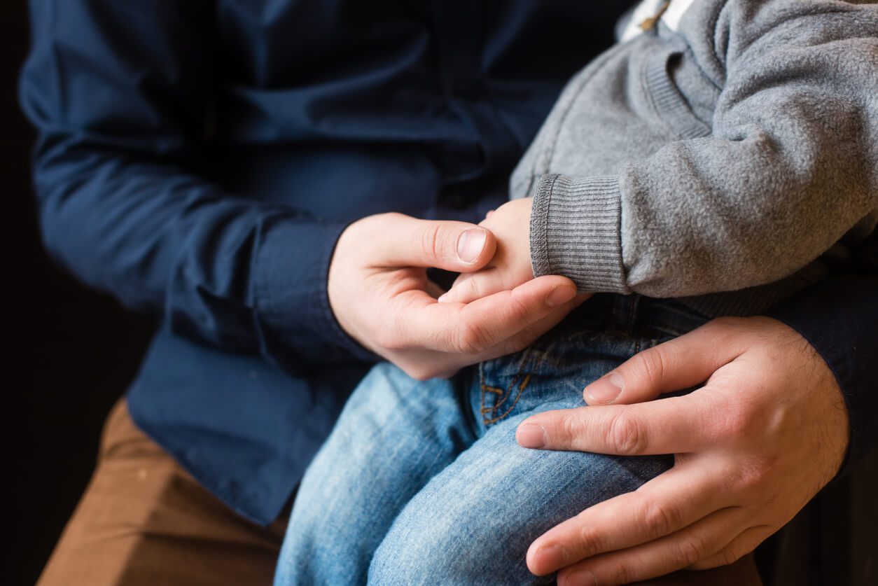 Close up of father's hands holding his child's hands, contact the Elmhurst child custody attorneys for help with your parenting time case.