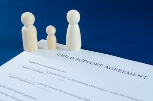 A wooden figurine family stands on a child support agreement document on the desk of an Oak Brook divorce attorney.