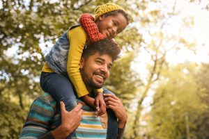 A man with his daughter on his shoulders during fall season, contact the Naperville child custody attorneys for help with your parenting time case.