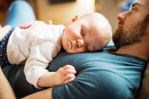 Man reclining with baby girl sleeping on chest, to receive child support from father hire an Elmhurst paternity lawyer.
