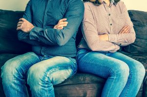 A couple with arms folded sitting back to back, when beginning divorce process meet with IL Divorce Lawyers for proper filings.