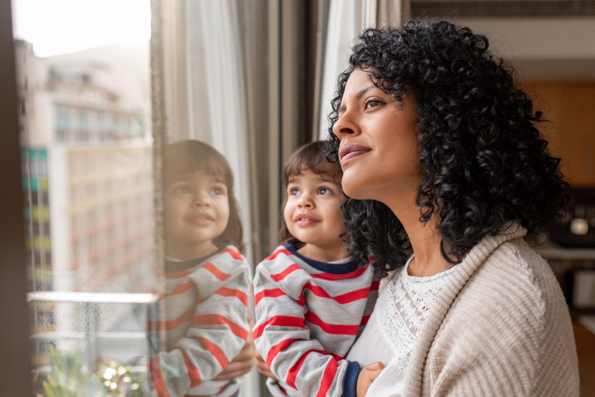 Woman holding little daughter looking out window, Illinois Divorce Attorney are able to help with child custody modifications.